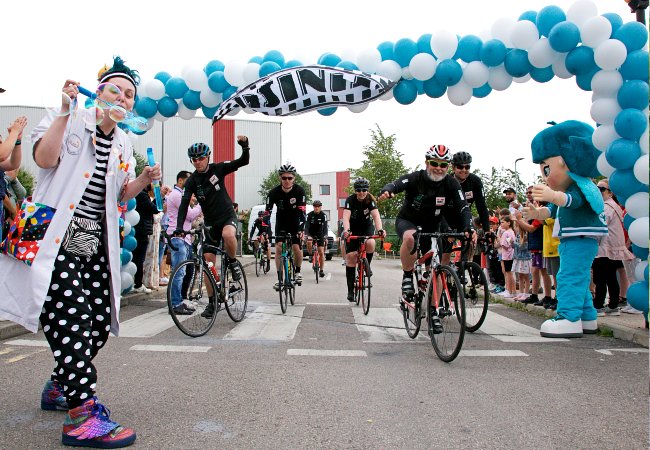Tour D'Alliance 2022 - Cyclists crossing the finishing line with a Giggle Doctor from Theodora Children's Charity